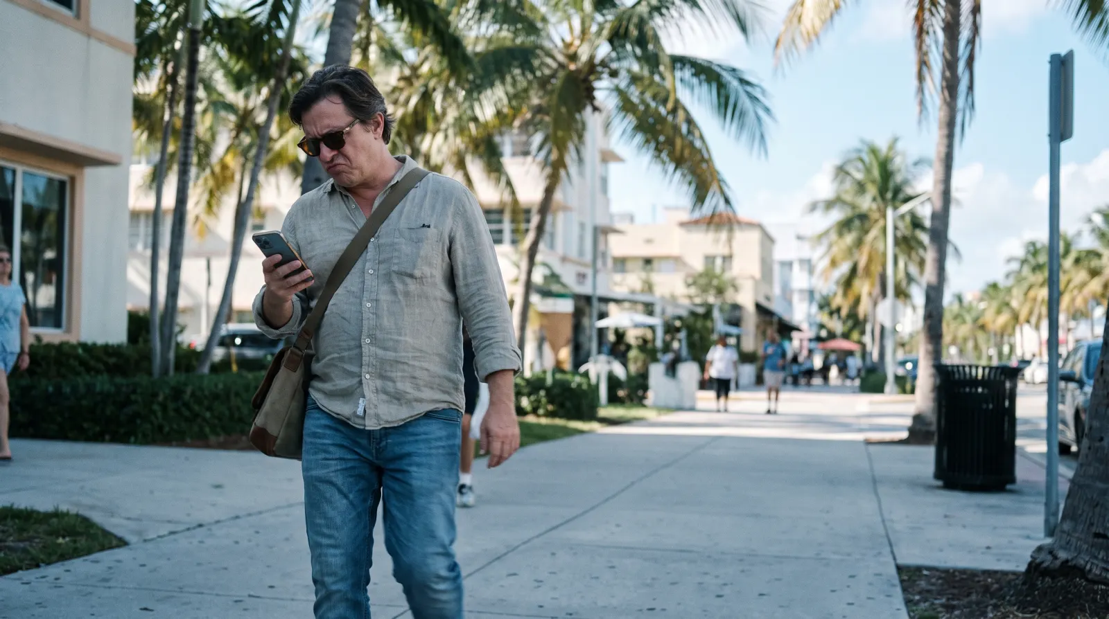 A person glancing impatiently at their phone while walking on a South Florida sidewalk.