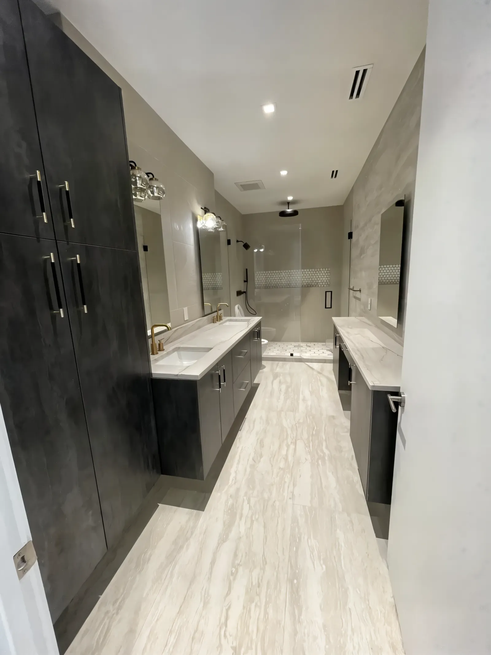 The same primary bathroom after the remodel with dark floor-to-ceiling cabinets, a floating double vanity and a glass shower